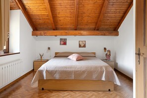 A bedroom with a wooden ceiling, a bed with a white quilt, a wooden bench, and two bedside tables with decorative items.