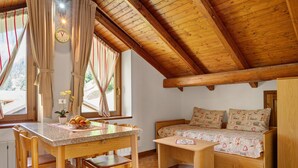 Una habitación acogedora con techo de madera, cama con ropa de cama estampada, una mesa de comedor con sillas y una ventana con cortinas.