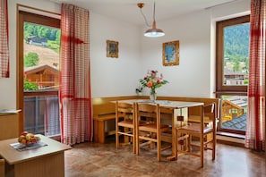 A dining area with a wooden table and chairs, a vase with flowers, and a view of a house through a window.