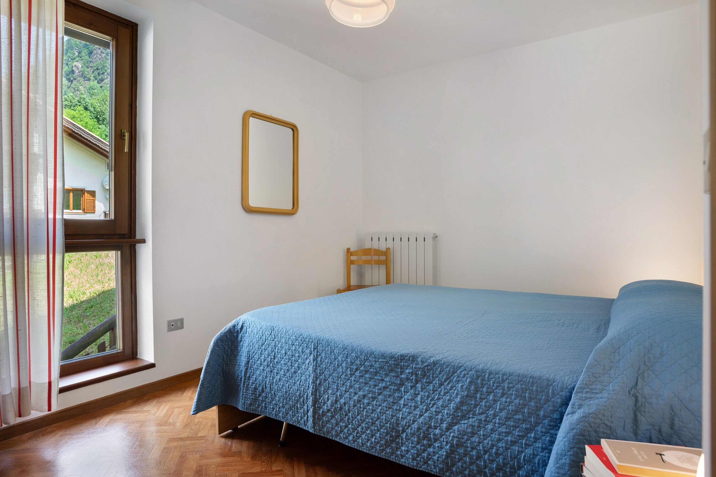 A bedroom with a bed, a window, a radiator, and a mirror.