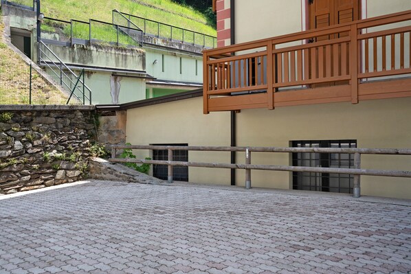 A courtyard with a stone wall, a wooden balcony, and a paved floor.