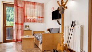 Ein Schlafzimmer mit einem hölzernen Bett, einem Schreibtisch, einem Fernseher und einem Kleiderständer mit Ski.