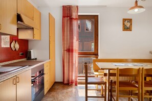 A compact kitchen with wooden cabinets, a built-in oven, and a dining area with a wooden table and chairs.