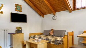 Ein gemütliches Zimmer mit einem Bett, einem kleinen Tisch, einem Stuhl, einem Fernseher, einer Uhr und einer Heizung.