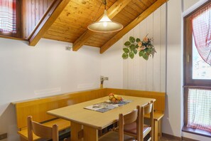 Un espace repas comprenant une table en bois, des bancs, un luminaire suspendu et une fenêtre donnant sur un paysage.