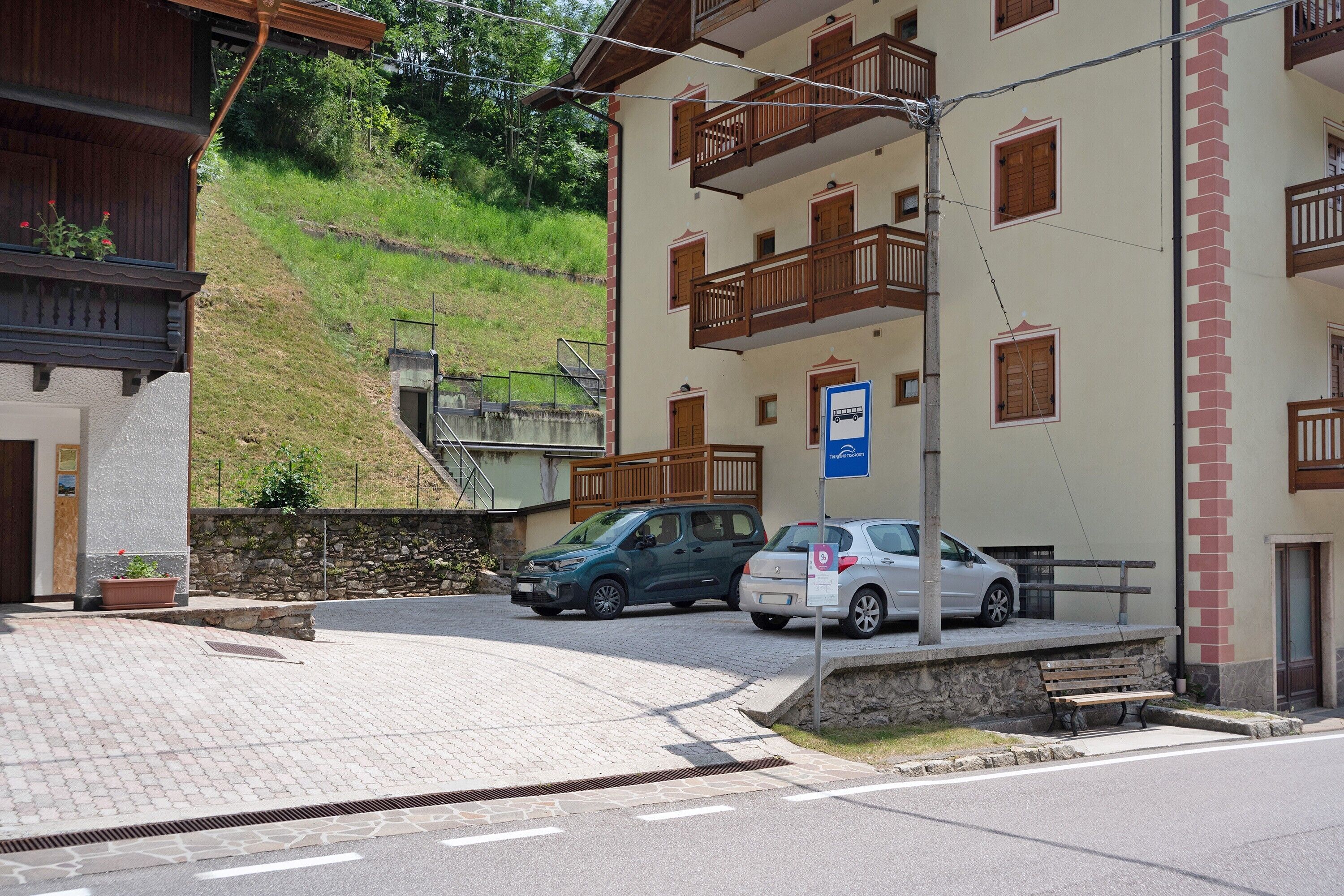 Un edificio con un muro de piedra, un área pavimentada y un coche estacionado frente a él.