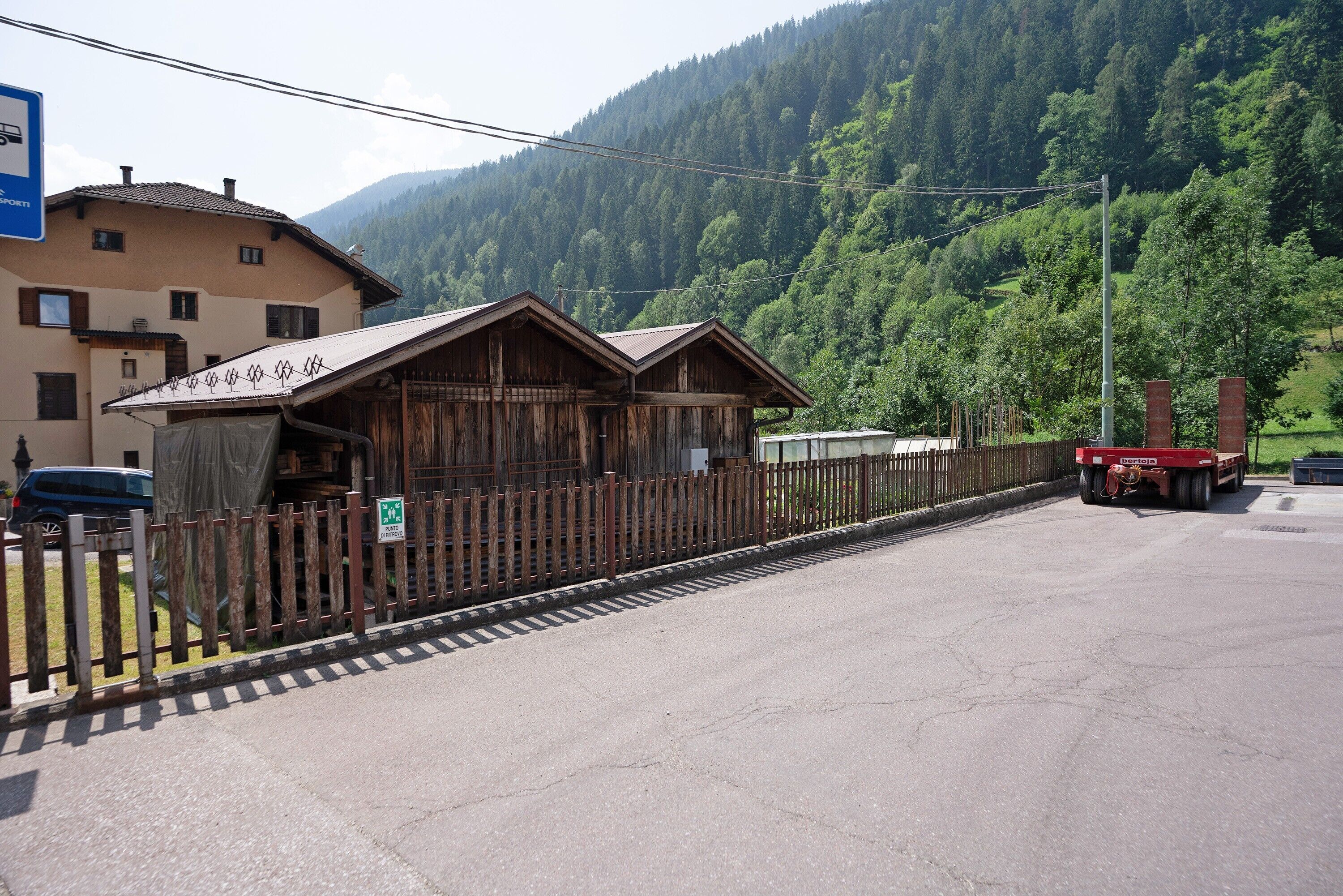Ein Holzhaus mit geneigtem Dach, einem umzäunten Bereich und einem Berg im Hintergrund.