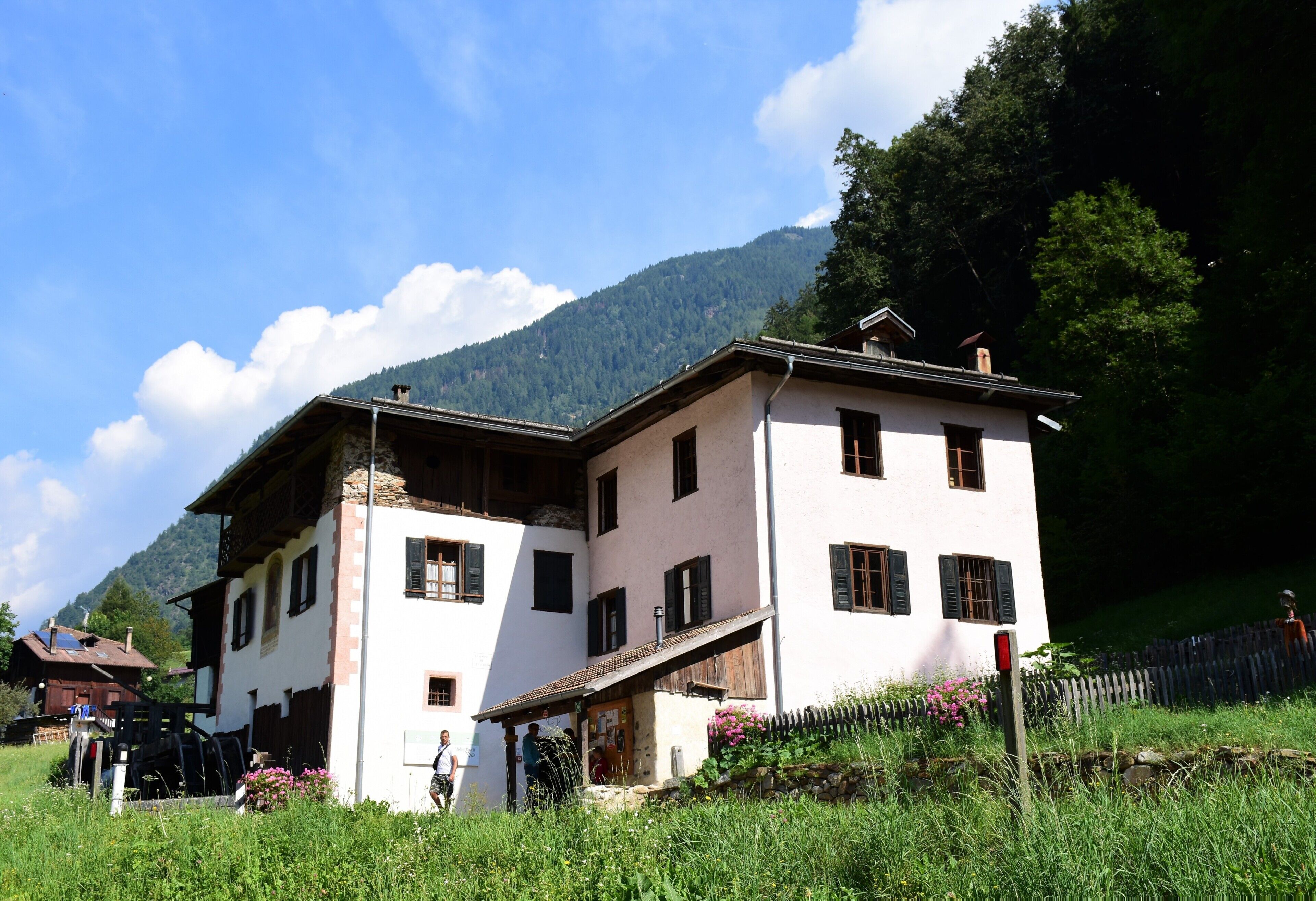 A traditional two-story building with a sloped roof, a balcony, and a small attached structure with a sloped roof.