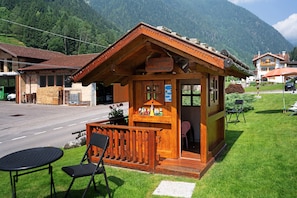 A wooden mountain lodge with a balcony, a small outdoor seating area, and a view of the surrounding mountains.