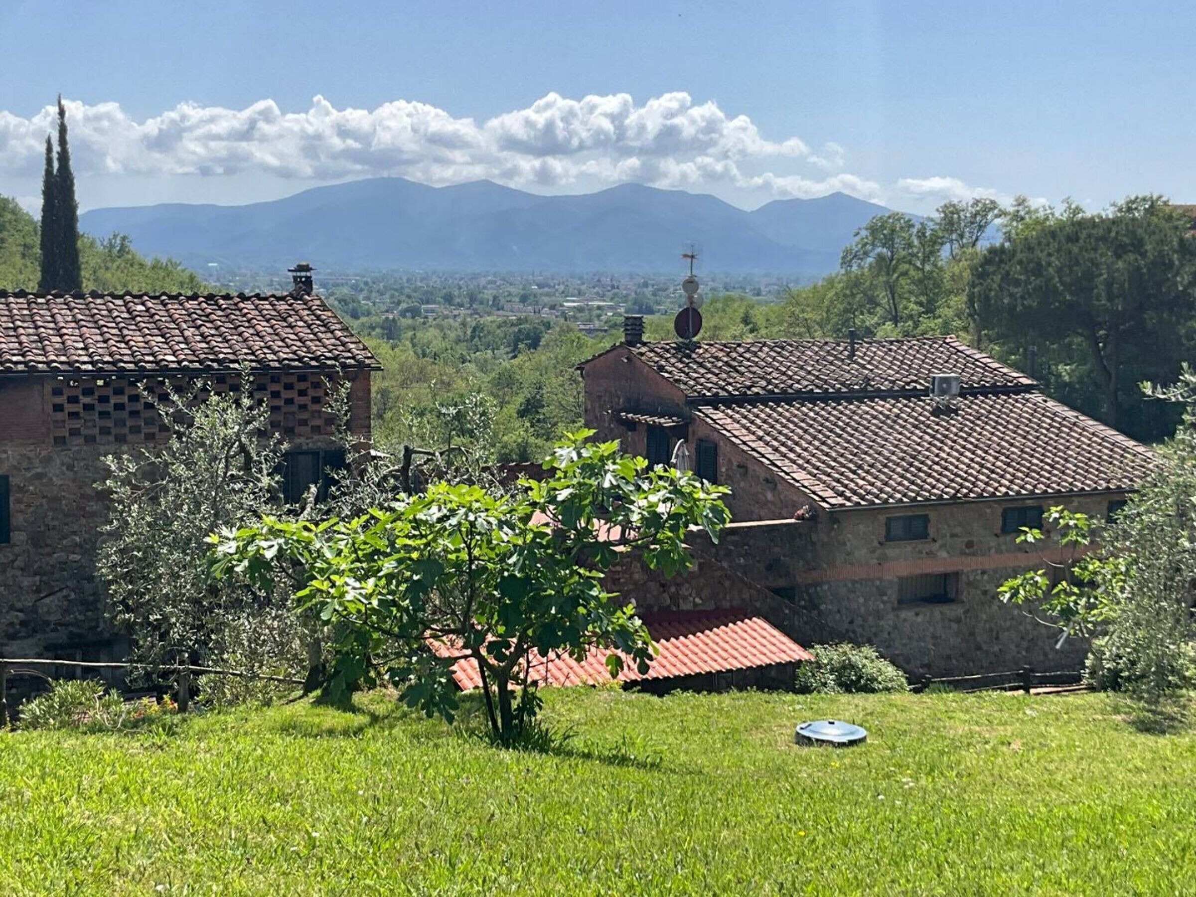 A rural landscape with stone buildings, a clear sky, and distant mountains.