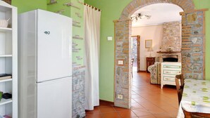 Une cuisine avec un réfrigérateur blanc, une arche en pierre, une table à manger recouverte d’une nappe verte et un four en briques.