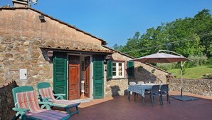 Un bâtiment en pierre avec une porte en bois, des volets verts et une terrasse avec une table et des chaises.