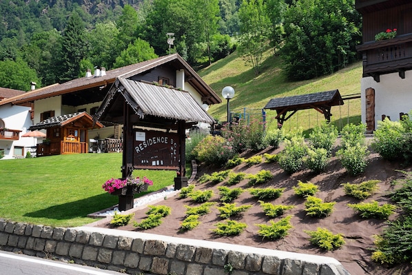 A traditional chalet with a wooden facade, a signboard, and a well-maintained garden with shrubs and flowers.