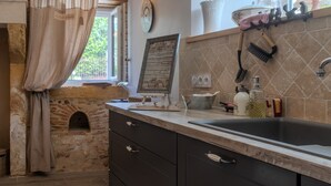 Una cocina con horno de piedra, un lavabo y varios utensilios.