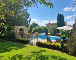 A swimming pool with a stone archway, surrounded by greenery and a stone building in the background. - L'Écrin de la Rose – Peaceful Retreat with Pool and Nature (Yvrac et malleyrand)