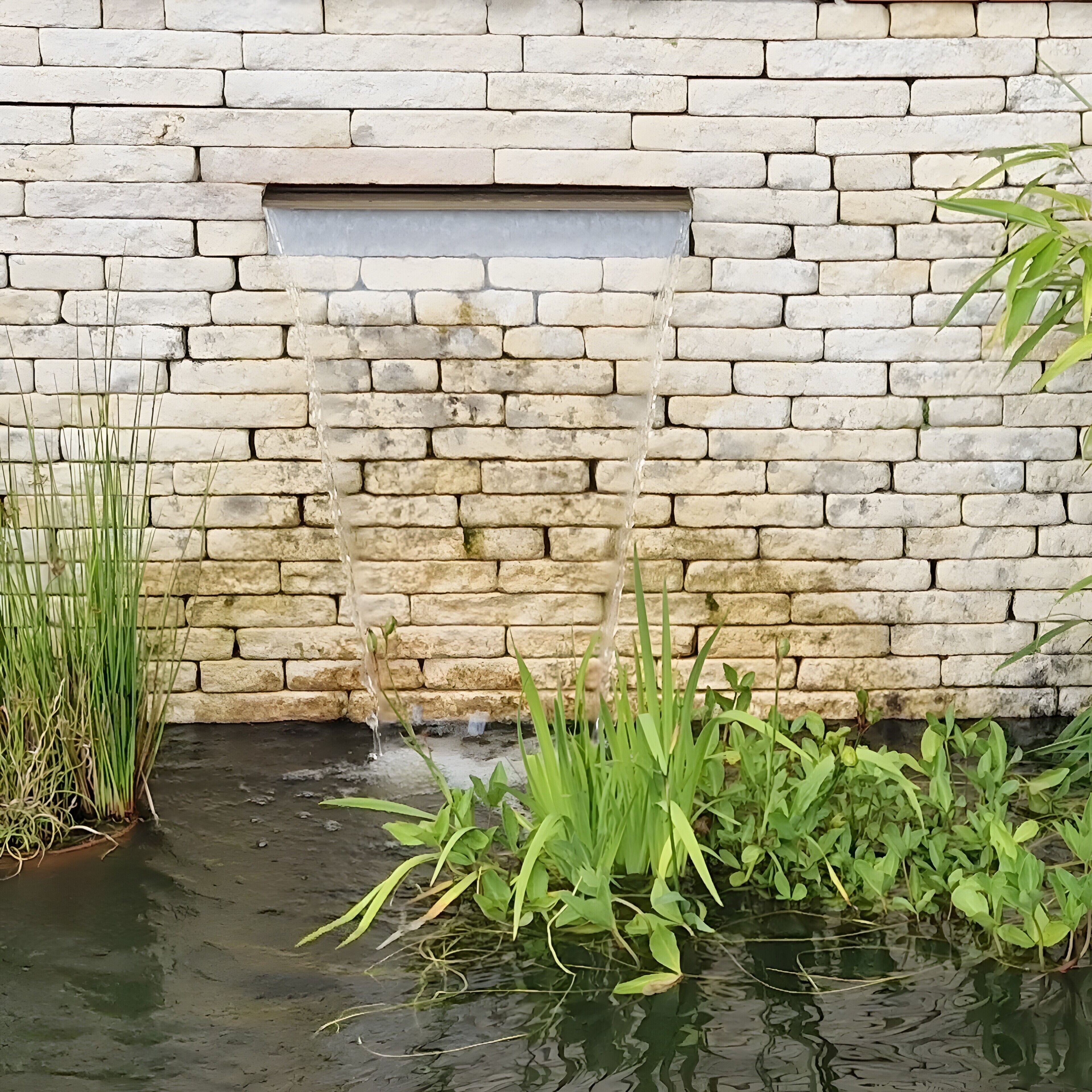 Un mur de pierre avec une petite fenêtre et un élément décoratif aquatique agrémenté de plantes.