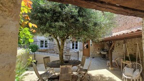 Un patio al aire libre con una mesa redonda y sillas, un sillón colgante y un árbol.