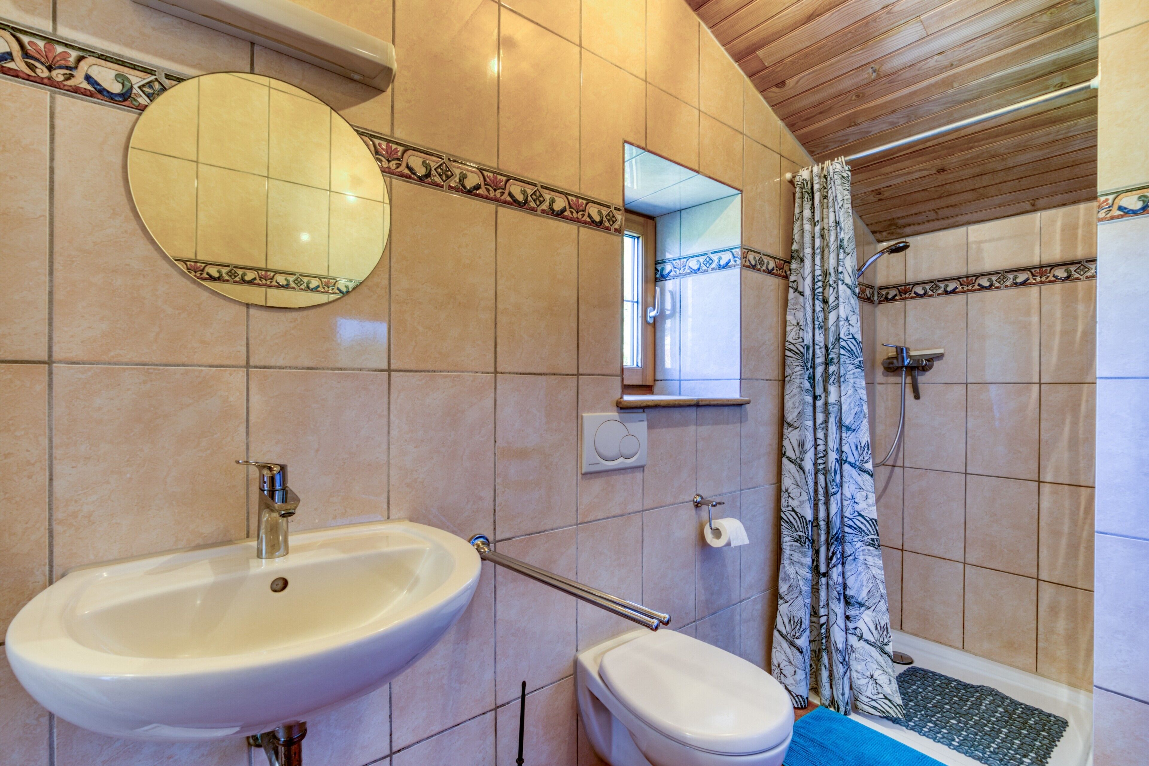 A bathroom with a sink, toilet, mirror, shower, and decorative tiles.