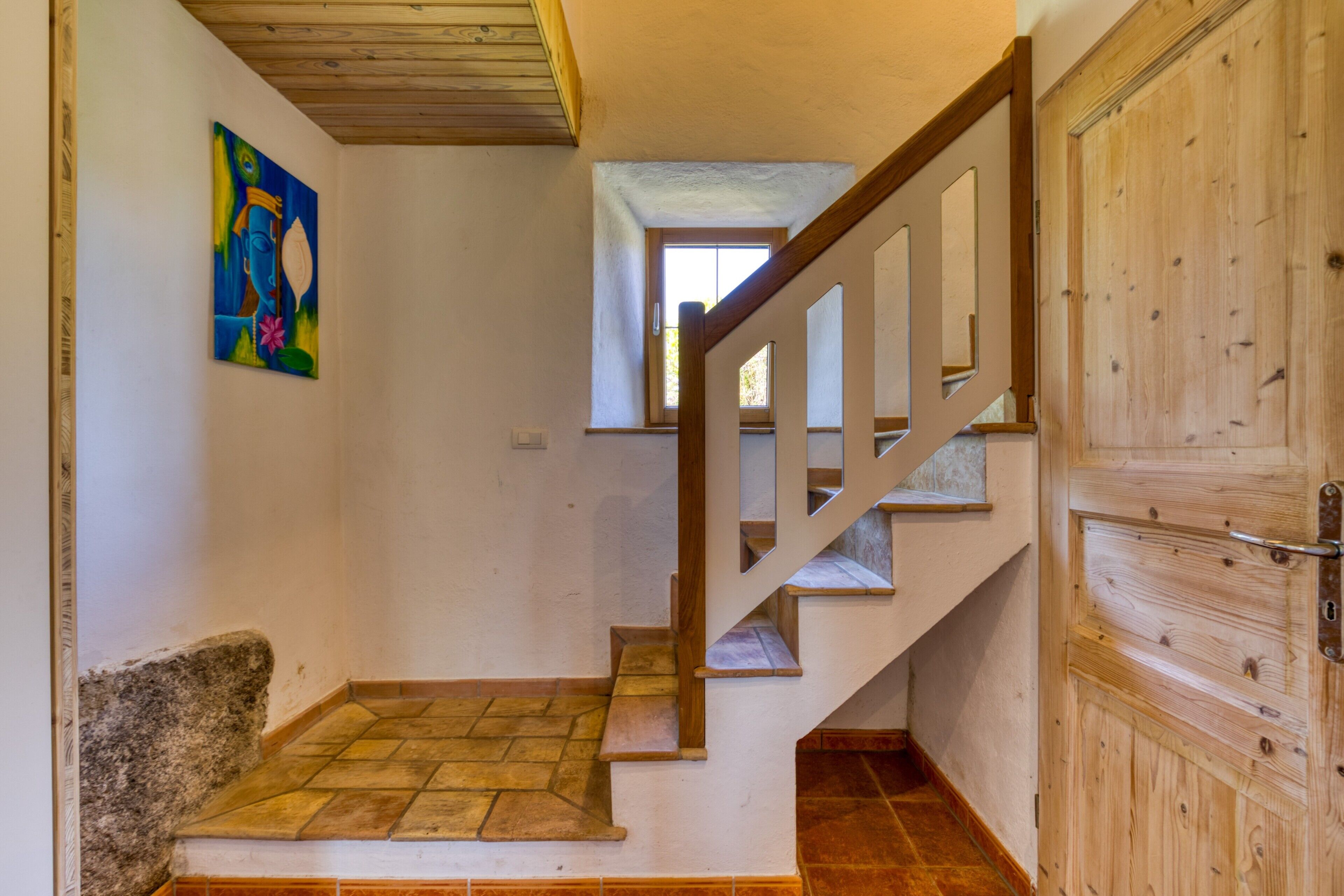 A staircase with wooden railings and a tiled floor leading to a door with a metal handle.