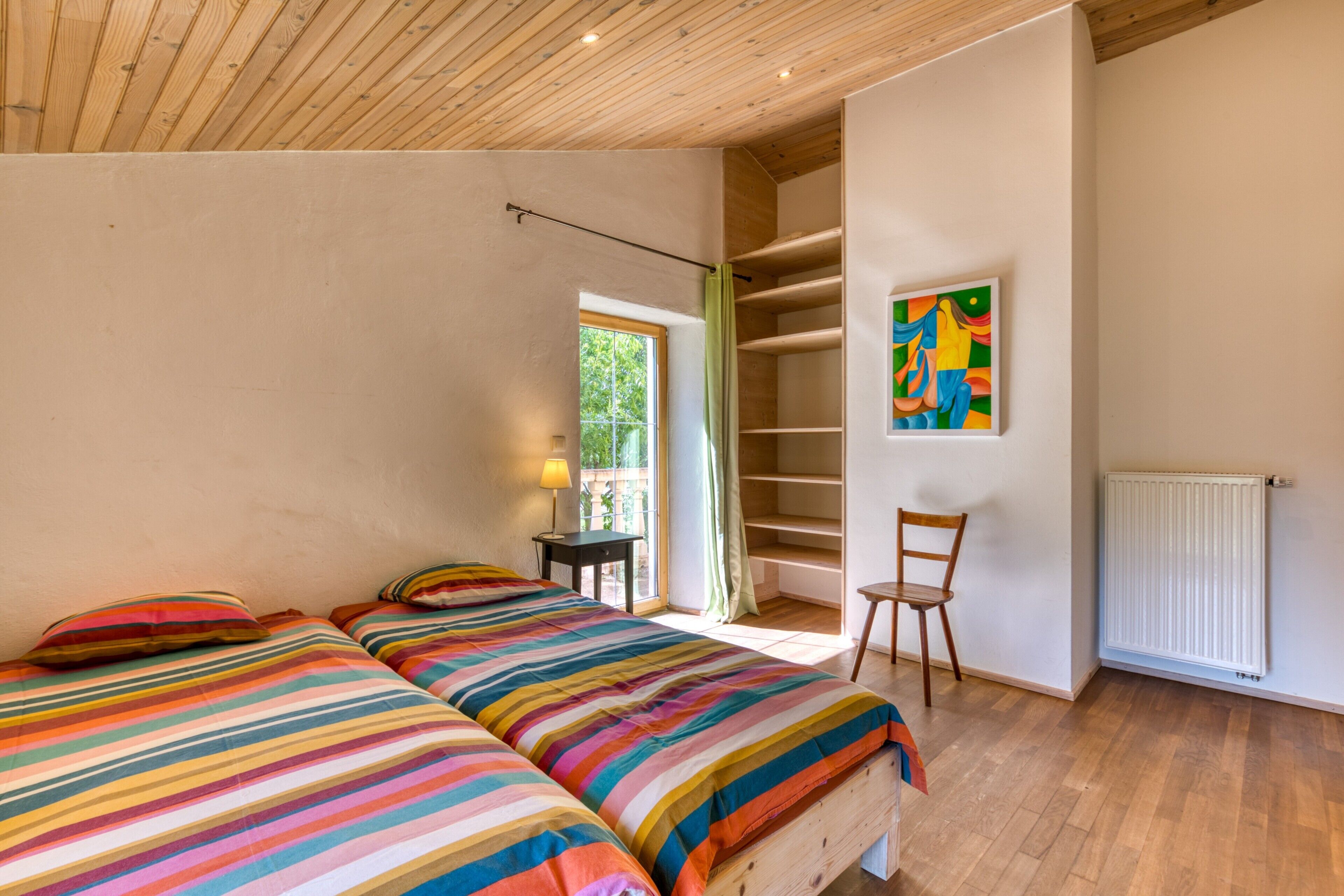 Un dormitorio con dos camas, una silla, un radiador y una ventana.