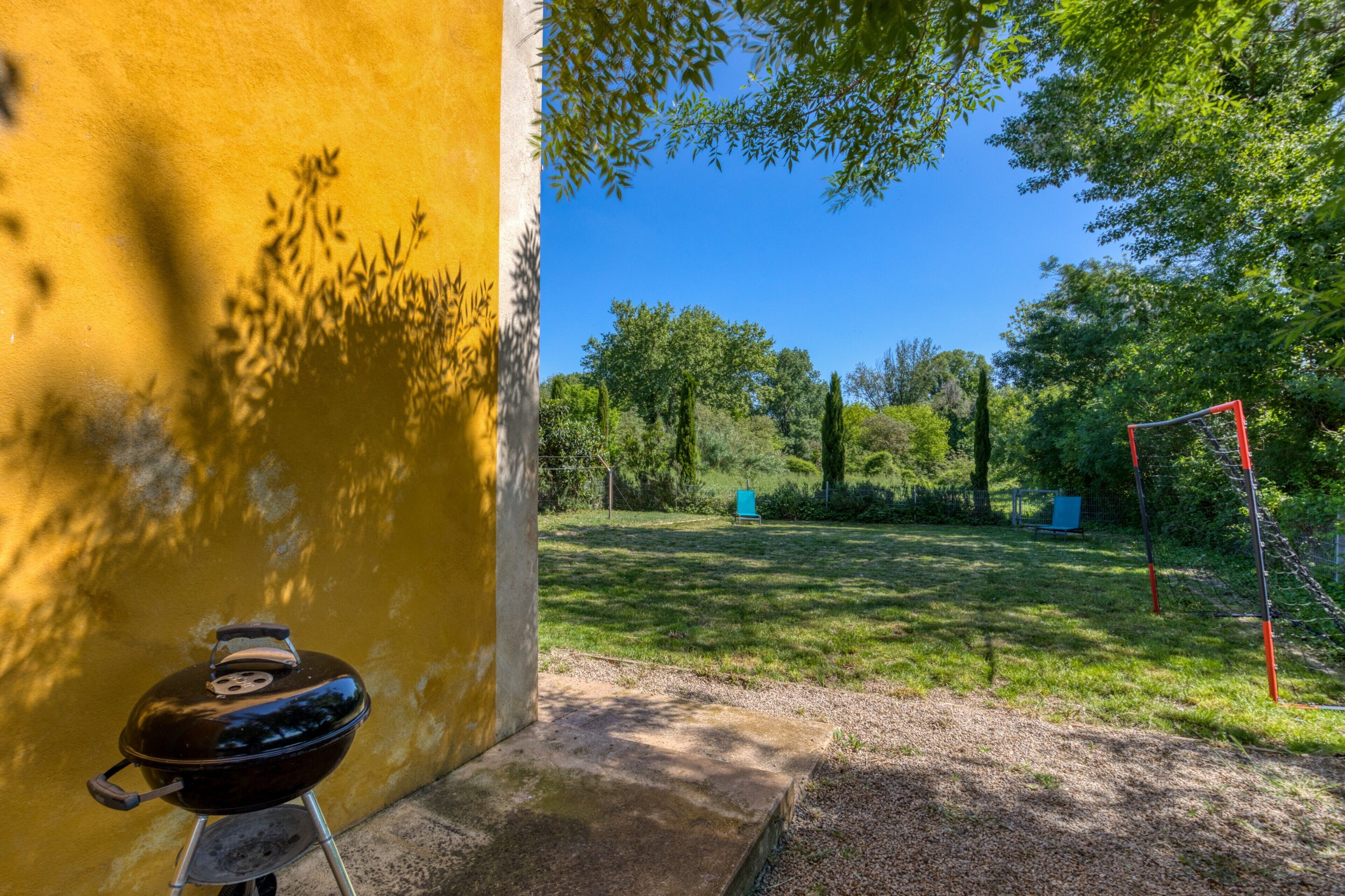 A backyard with a barbecue grill, a yellow wall, and a soccer goal.
