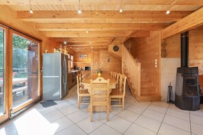 A wooden interior with a dining table, chairs, a kitchen area, and a fireplace.