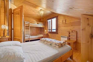Ein Schlafzimmer einer Holzhütte mit Etagenbetten, einem Einzelbett, einem Fenster und einer Heizung.