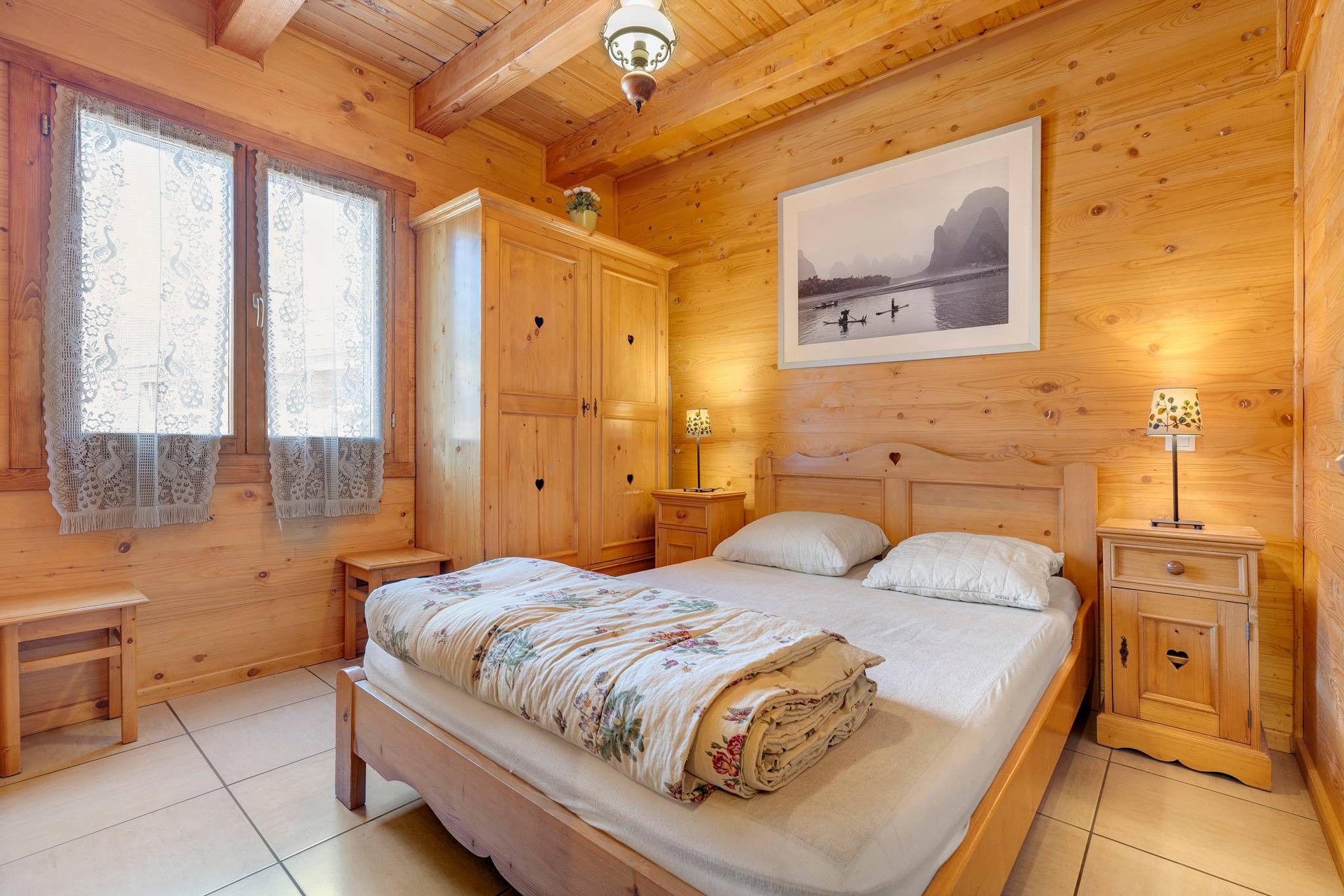 Quarto de madeira com cama, mesas de cabeceira, cômoda e um quadro na parede.