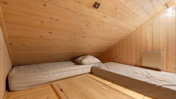 Een kleine kamer met houten lambrisering, twee eenpersoonsbedden en één lamp.