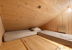 Ein kleiner Raum mit Holzwänden, zwei Einzelbetten und einer Lampe.