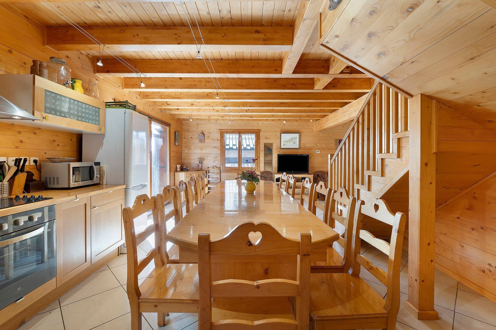Interior em madeira com mesa de jantar, cadeiras, área de cozinha com eletrodomésticos e escada.