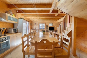 Interior em madeira com mesa de jantar, cadeiras, área de cozinha com eletrodomésticos e escada.