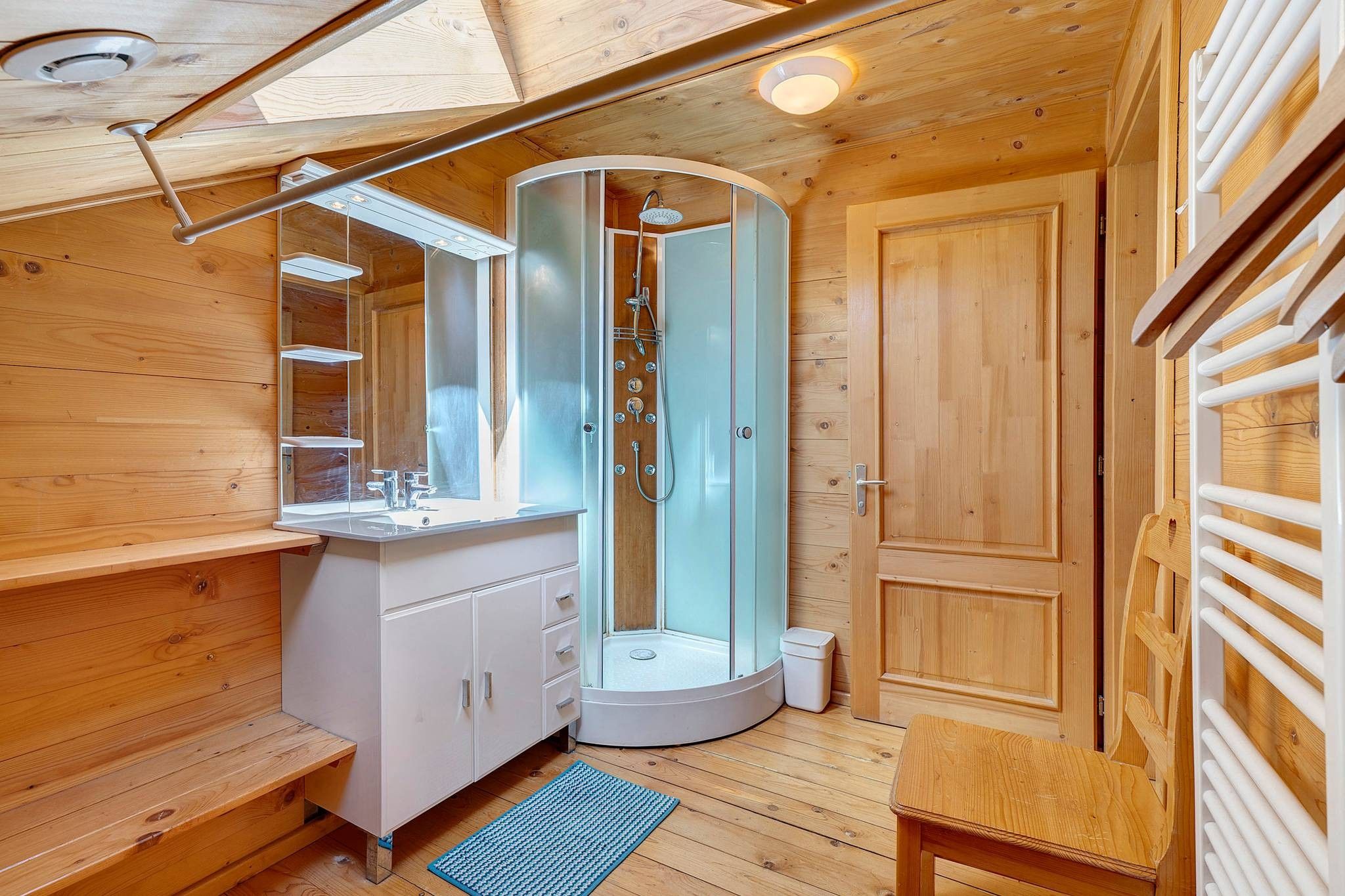 Een klein, houten badkamer met een douche, wastafel en kastjes.