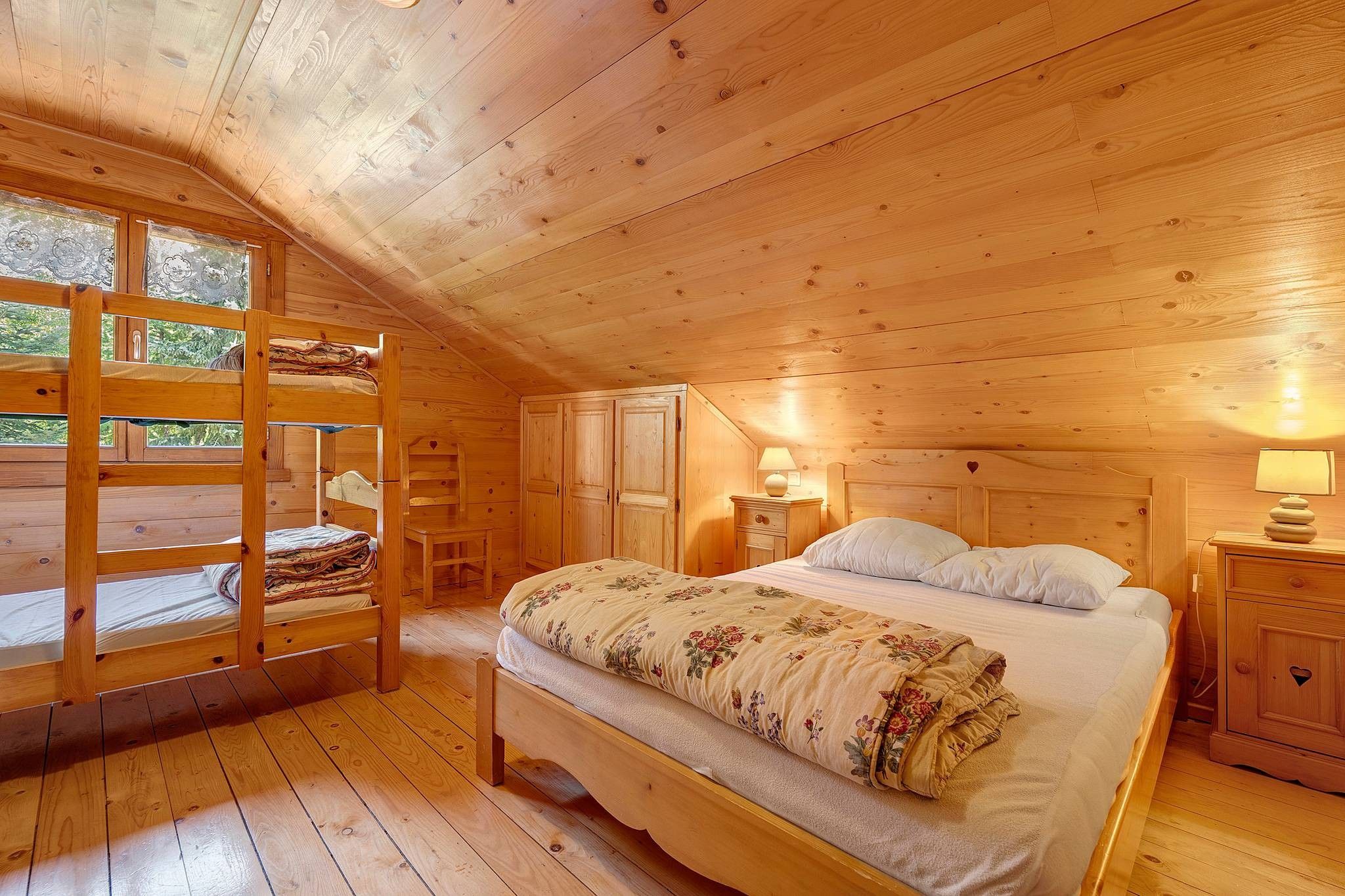 Un dormitorio de cabaña de madera con una litera, una cama individual, un aparador y una mesita de noche.