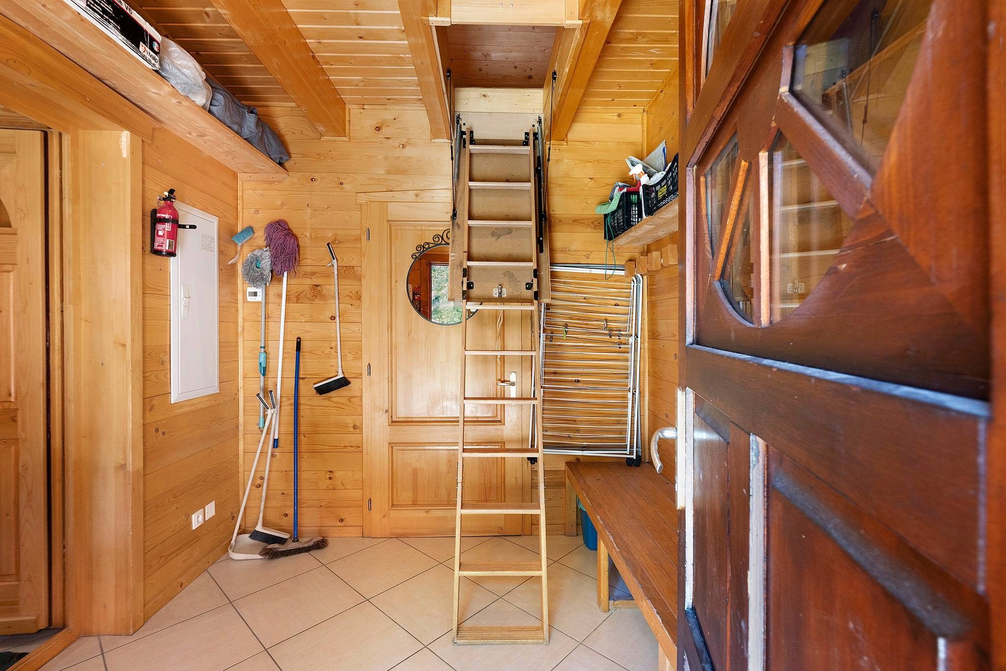 Interior em madeira com escada central, quadro branco e materiais de limpeza.