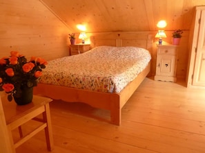 A wooden room with a bed, bedside tables, a nightstand, a cabinet, and a vase with flowers. - Chalet 'Deux Grands Chalets Communicants' with Mountain View, Shared Pool and Wi-Fi (Les Orres)