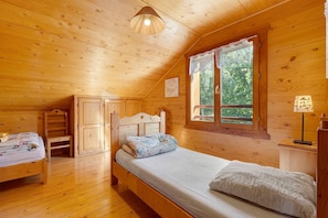 Quarto de cabana de madeira aconchegante, com uma cama de solteiro, cômoda, mesa de cabeceira e janela com vista para o verde.