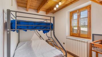 A bunk bed with a mattress, a wooden ceiling, a window with blinds, and a radiator.
