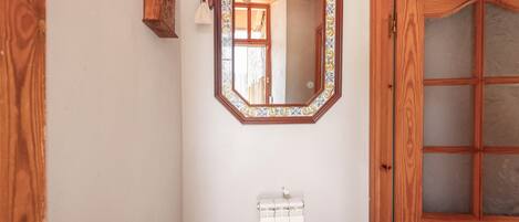 Une salle de bain avec une porte en bois, un miroir doté d’un cadre décoratif, un porte-serviettes et un radiateur.