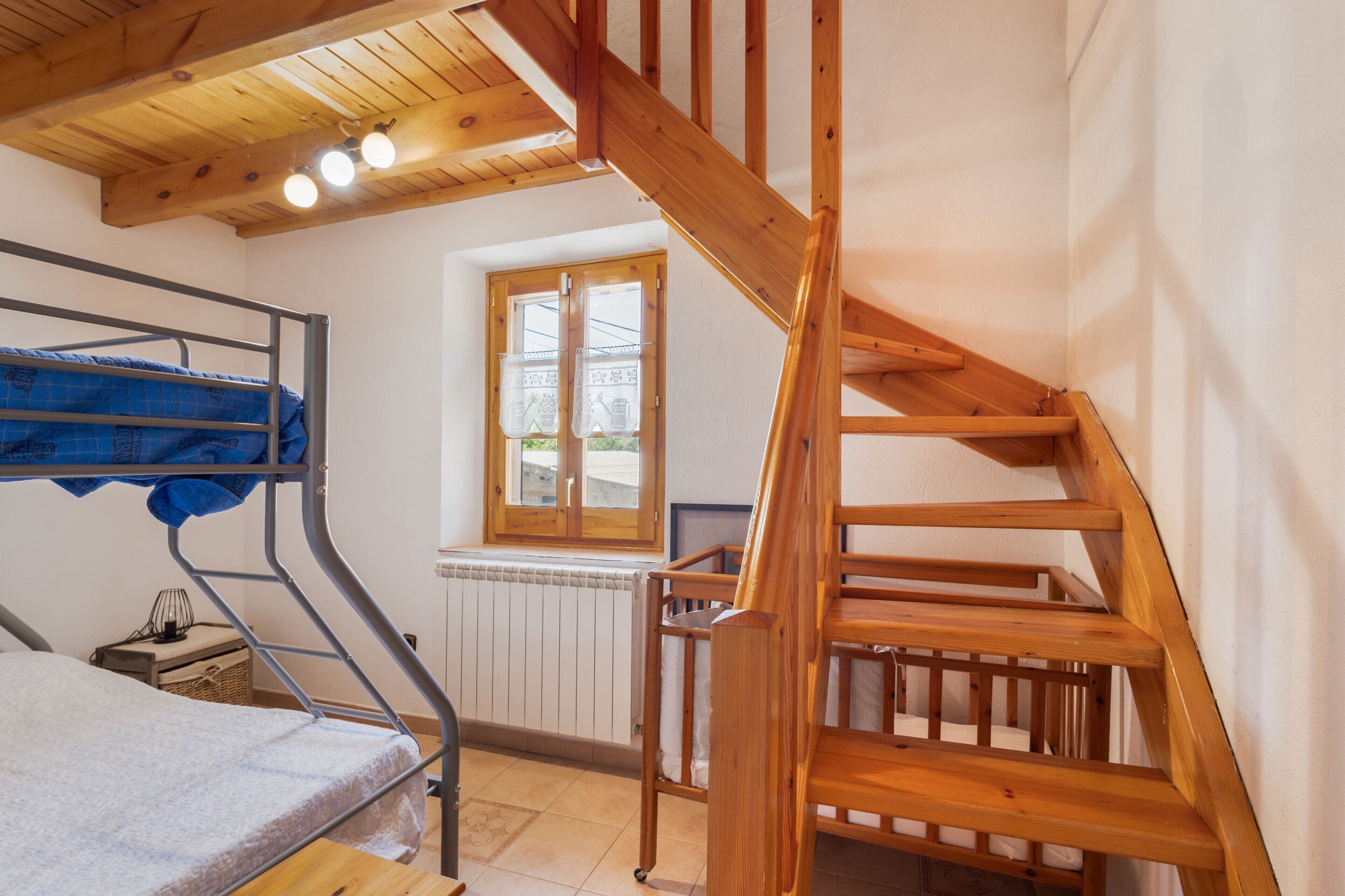 Una habitación con una cama litera, una escalera de madera, una ventana con vistas y un radiador.