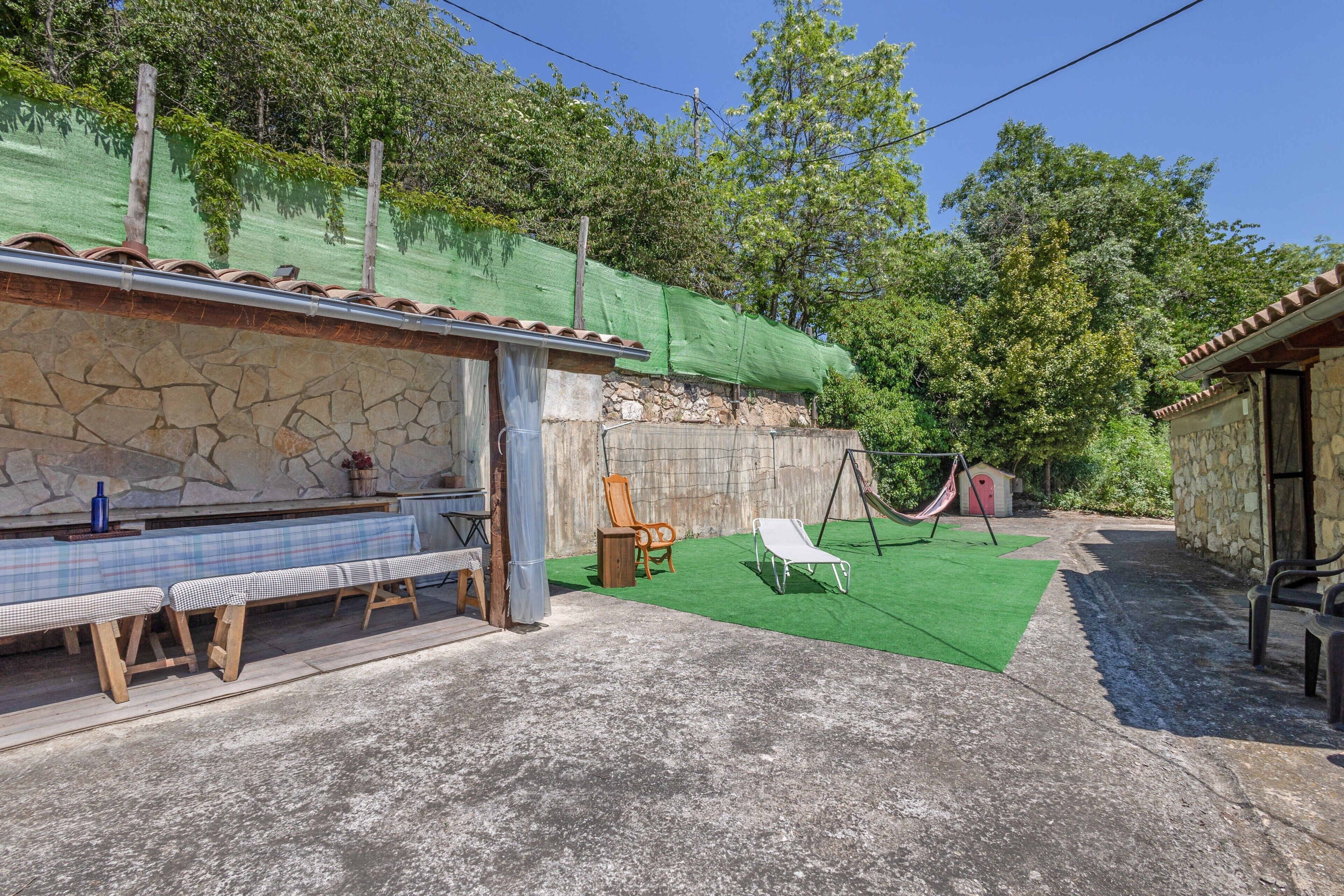 Ein Patio mit einer Steinmauer, einer Bank, einer Hängematte und einem Tisch mit kariertem Tischläufer.