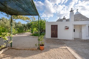 Un edificio blanco con puerta marrón, camino de grava y pérgola verde.