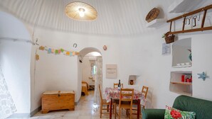 Ein gemütliches Zimmer mit einer Holzkiste, einem Esstisch mit Stühlen, einer grünen Couch und einem hängenden Korb.