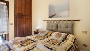 Een slaapkamer met een bed, een houten garderobe, een nachtkastje, een lamp en een schilderij aan de muur.