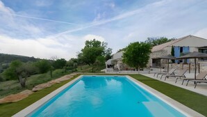 Ein rechteckiger Swimmingpool mit glasklar blauem Wasser, umgeben von einer gepflegten Rasenfläche und einigen Bäumen.