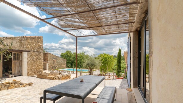 Eine Terrasse im Freien mit Tisch und Bänken, Steinmauern und Blick auf ein Schwimmbecken.