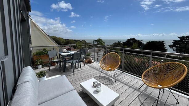 A balcony with a white table, two wicker chairs, a sofa, and potted plants. - Ocean View XXL Terrace – Premium (Pornic)