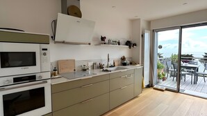 A modern kitchen with built-in appliances, a large window, and a view of the outdoors. - Ocean View XXL Terrace – Premium (Pornic)