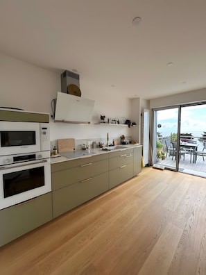 A modern kitchen with built-in appliances, a large window, and a view of the outdoors. - Ocean View XXL Terrace – Premium (Pornic)