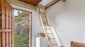 Una habitación con puerta de madera, un refrigerador blanco, una mesa de madera y una escalera de madera apoyada en la pared.